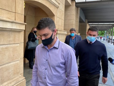 Dua pria muda mengenakan masker wajah berjalan di sepanjang jalan setapak di luar gedung pengadilan