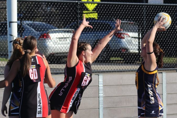 A woman in black and red Goal Keeper netball uniform defends against an opposing player taking a shot at goal