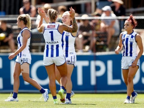 North Melbourne AFLW players high-five to celebrate a goal against Richmond.