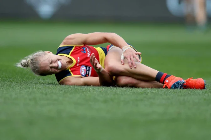 An AFLW player lies on the turf, clutching her knee after being injured in the 2019 grand final.