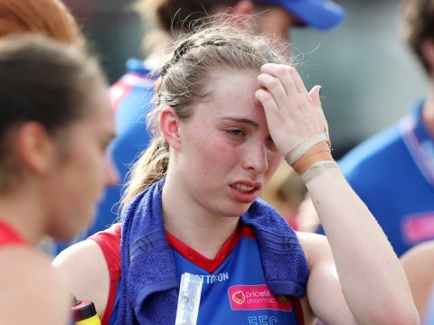 A tired and heat-affected AFLW player puts her hand to her forehead as she wears an ice towel around her neck.