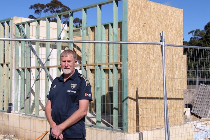 A man with greying hair and a beard stands with a construction site behind him.