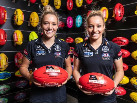 Two identical twin sisters hold footballs in their Carlton gear ahead of 2019 AFLW grand final week.