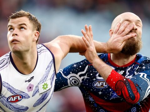 A Fremantle AFL player puts his left hand in the face of a Melbourne opponent.