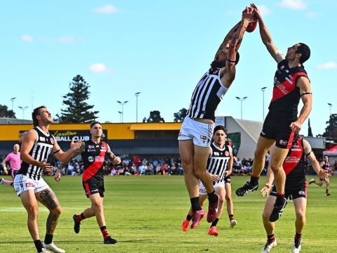 Charlie Dixon goes up for a mark, blue skies, footballers around, big arm stretch, black and white guernsey
