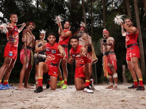 Gold Coast players wearing the club's Indigenous round jersey with men in ceremonial clothing and body paint.