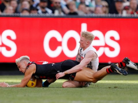 A Collingwood AFL player wraps his arms around the waist and hips of an Essendon player after bringing him to ground.