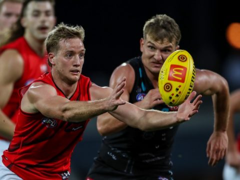 An Essendon AFL player is chased by a Port Adelaide opponent.