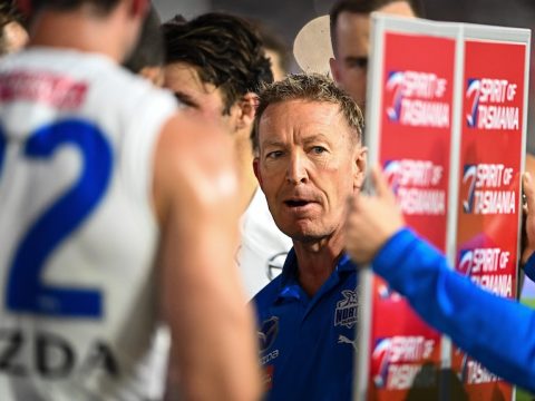 An AFL coach looks at a magnet board as he speaks to players at quarter-time during a match.