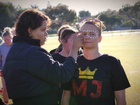 A woman applies white dot paint to another woman's face