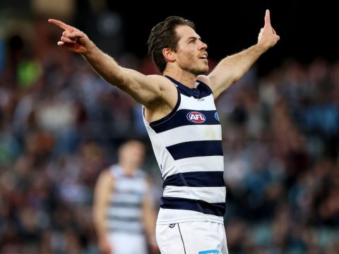 A Geelong Cats AFL player stands with his arms outstretched as he celebrates a goal.