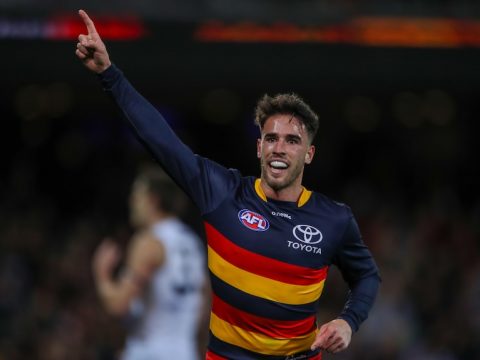 An Adelaide Crows AFL player points to the sky with his right hand.