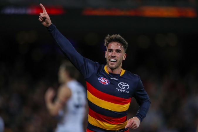 An Adelaide Crows AFL player points to the sky with his right hand.