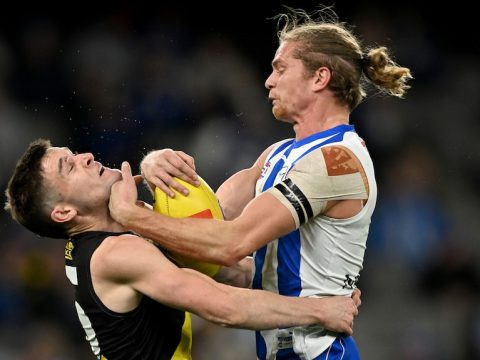 A Richmond AFL player tackles a North Melbourne opponent holding the ball.