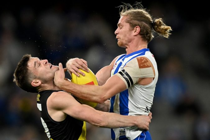 A Richmond AFL player tackles a North Melbourne opponent holding the ball.