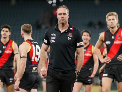 Essendon coach Ben Rutten looks stony-faced as his dejected players stand behind him after a big loss.