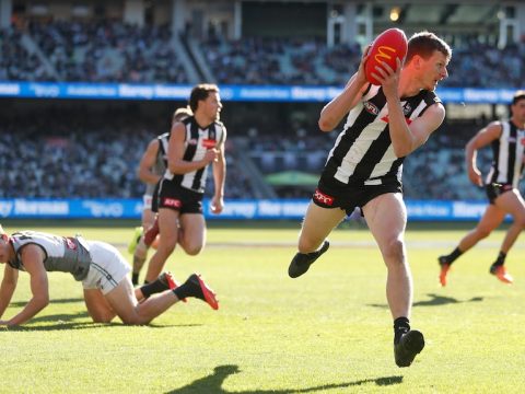 A Collingwood player turns and looks upfield after taking possession as a number of his teammates begin to run in support.