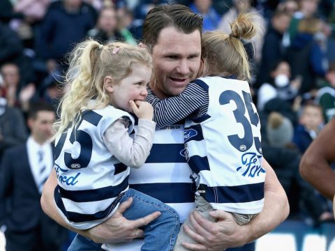 A Geelong AFL player holds his two daughters before a match.