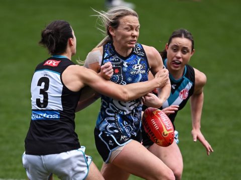 A Carlton AFLW player drops the ball while being tackled by a Port Adelaide opponent.
