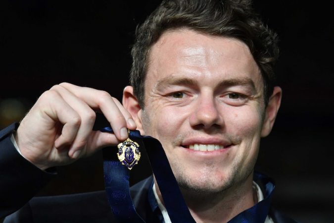Lachie Neale smiles while holding up his Brownlow Medal