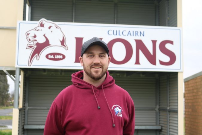 A man in a maroon jumper standing in front of the Culcairns Lions sign