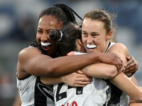 Three Collingwood AFLW players embrace as they celebrate a goal.