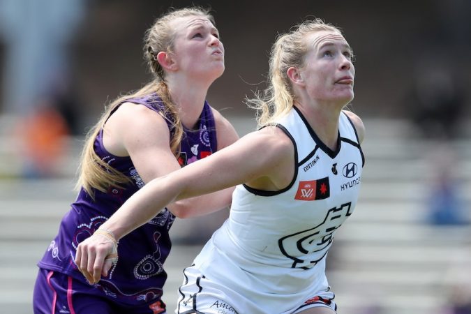 A Fremantle AFLW player contests for the ball alongside a Carlton opponent.