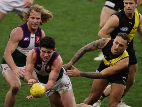 A Dockers player releases a handball under pressure as a Richmond player tries to grab him.