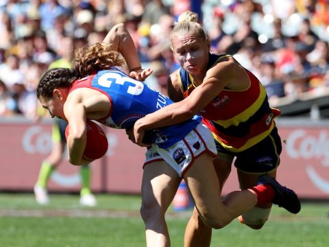 An AFLW player struggles to get free as she carries the ball, while an opponent grabs her in a tackle.