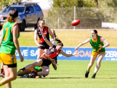 A woman is tackled to the ground in a game of footy
