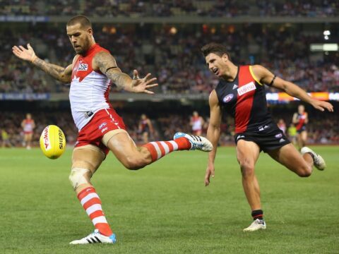 Sydney's Lance Franklin runs away from an Essendon defender and drops the ball to kick it long towards goal.