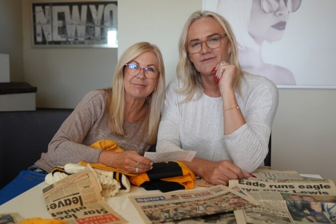 Danielle Laidley and partner Donna Leckie sit on a table with newspaper clippings of Danielle's AFL highlights in front of them.