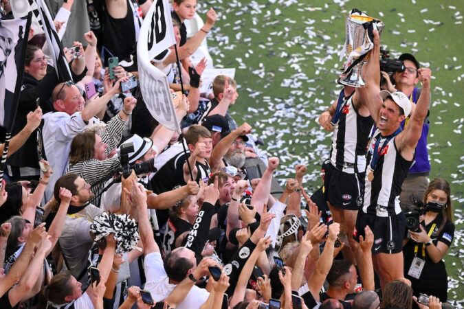 Scott Pendlebury stands on the fence and holds the cup aloft in front of Magpies fans