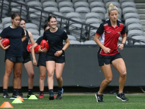 A woman leads the way in a running drill while junior players look on