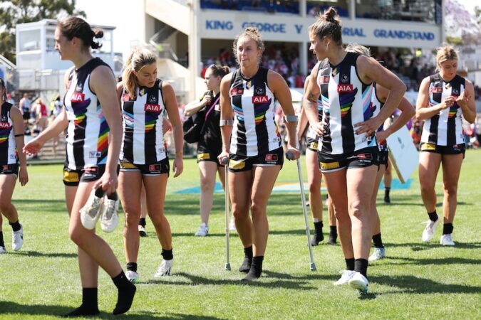 A Collingwood AFLW player leaves the ground on crutches surrounded by her teammates.